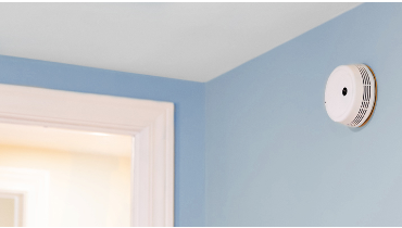 Close-up of smoke detector on sky blue wall.