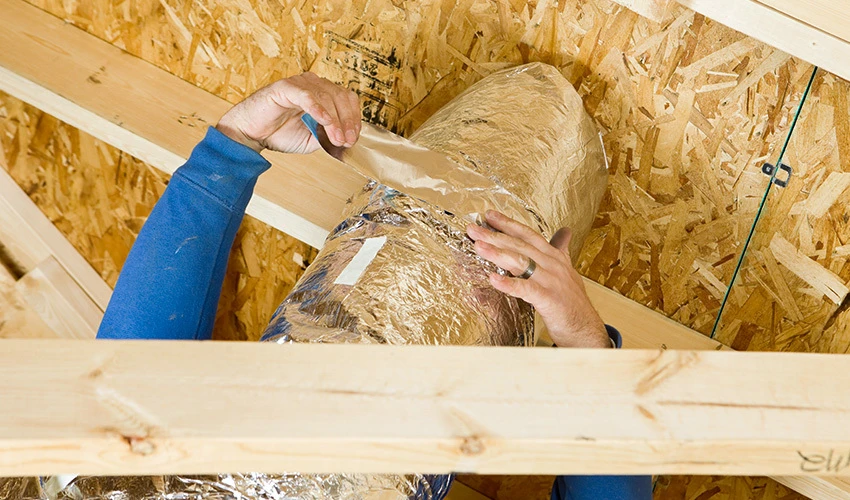 Close-up of Aire Serv technician installing air duct insulation.