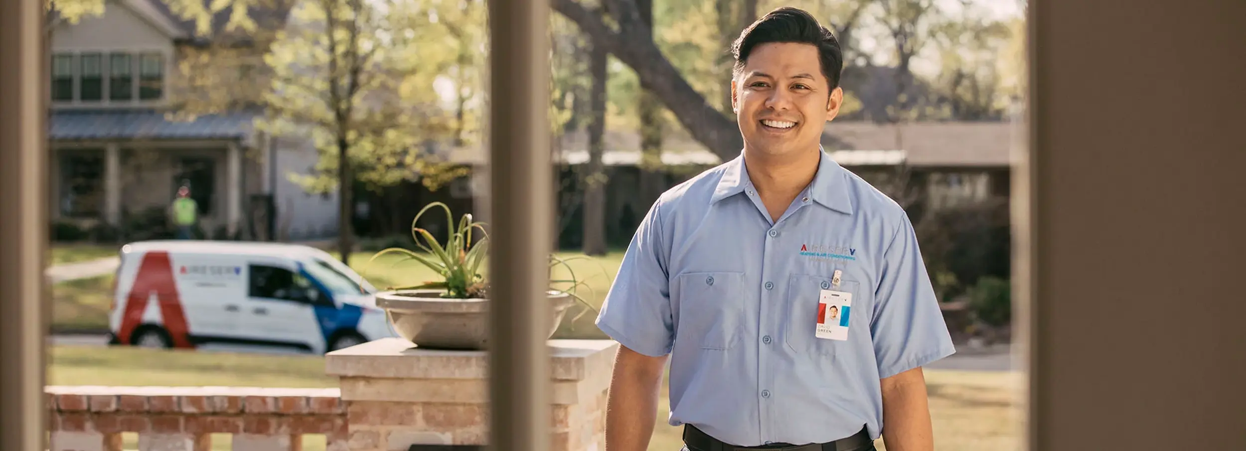 Smiling male Aire Serv technician in branded blue collared shirt arriving for residential service call.