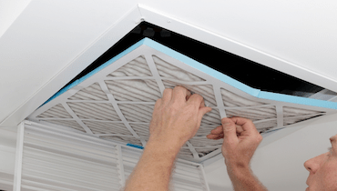 Man removing old air filter from ceiling intake vent of home HVAC system.